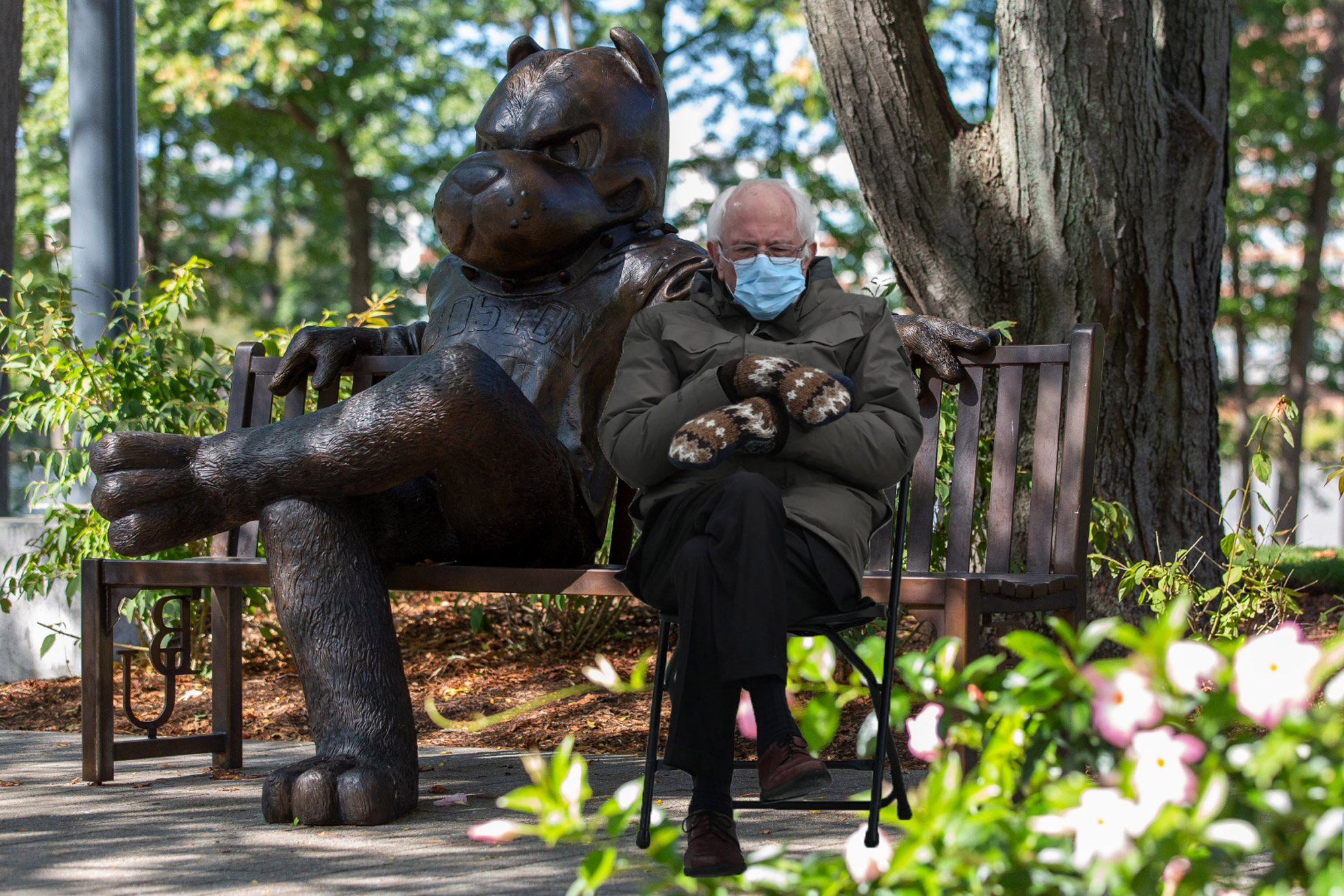 A photo of Bernie Sanders sitting with mittens and a jacket on next to the statue of Rhett on a bench on BU Beach.