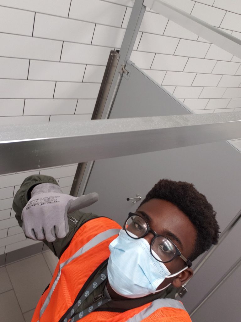 A photo of Olujimi Taiwo wearing a mask and orange vest while giving a thumbs up to the camera