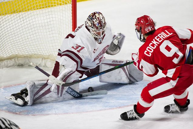 Photo of BU Men’s Hockey Captain Logan Cockerill (SHA’21) as he nearly scores a goal on the UMass goalie who tries to block the shot with his knee pads.