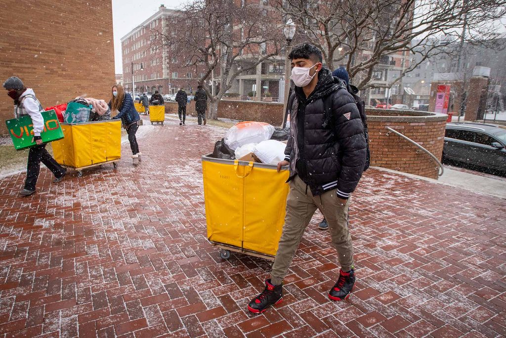 Photo of Ayush Kadakia (ENG’24) towing a yellow cart as he brings his things to move back into his West Campus dorm on January 21, 2021. He wears a black coat and face mask as snow gathers on the sidewalk.