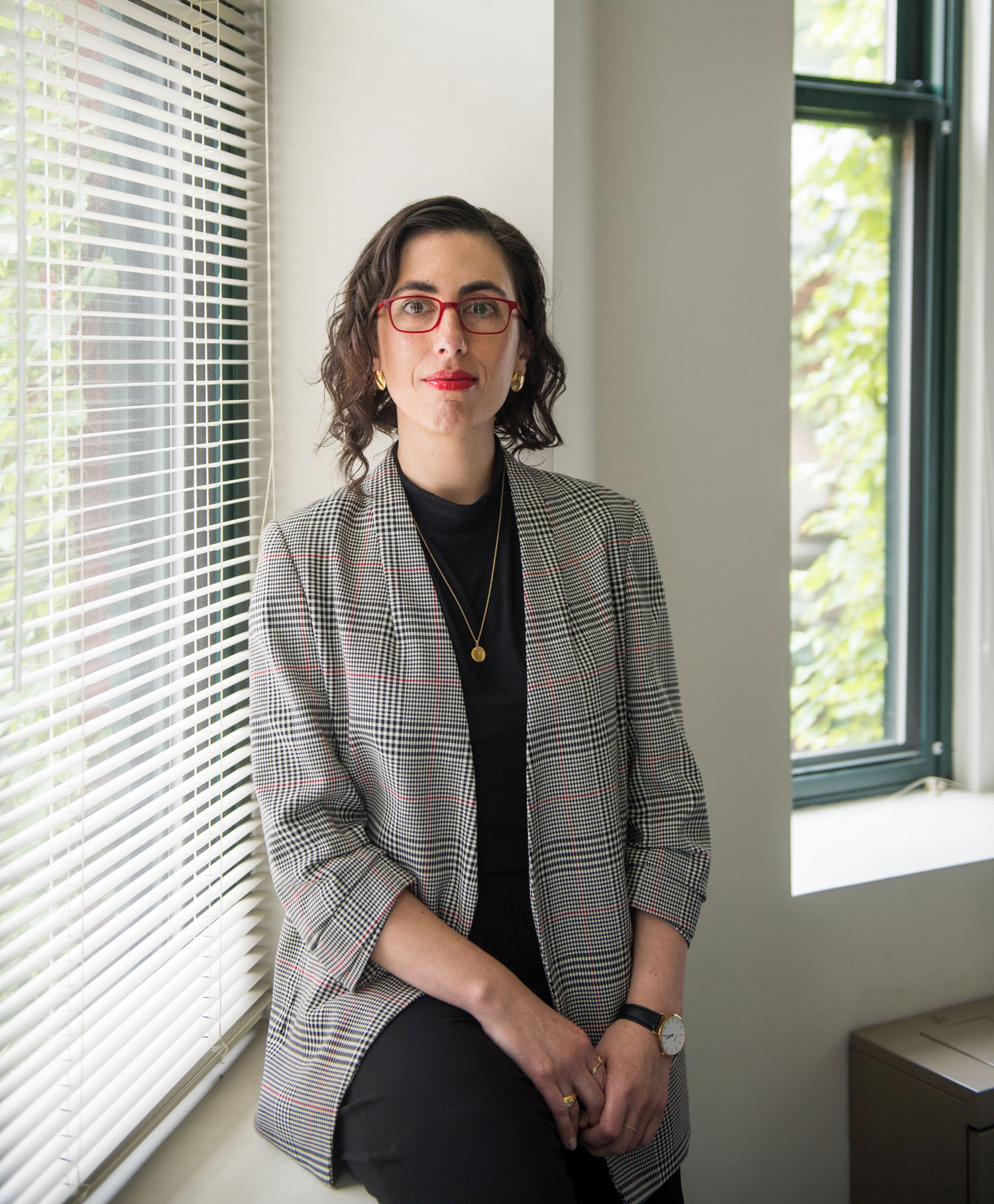 A portrait photo of Sarah Lipson sitting on a window ledge