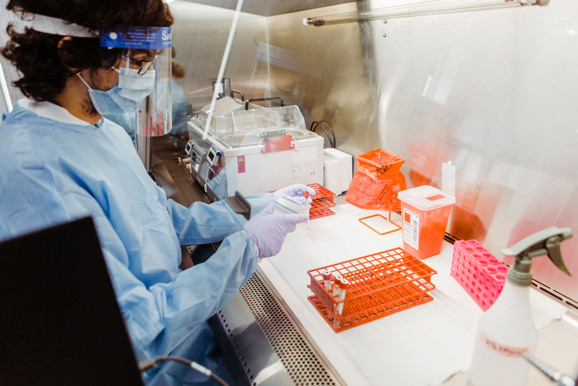 A photo of the clinical testing lab at BU. A woman stands in protective gear handling testtubes.