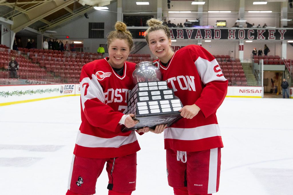 Jesse Compher with teammate Abby Cook holding the Beanpot trophy on the ice