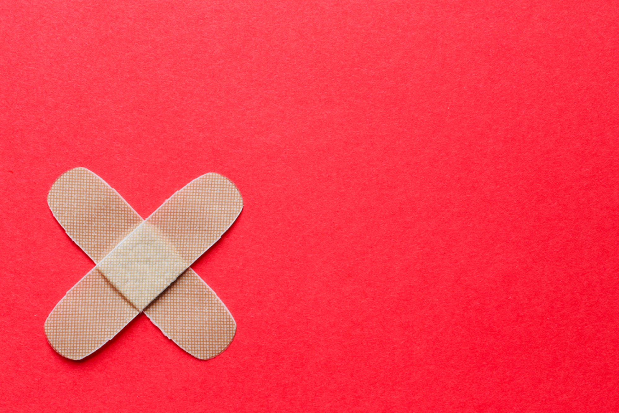 A photo of a pair of crossed bandaids over a red background