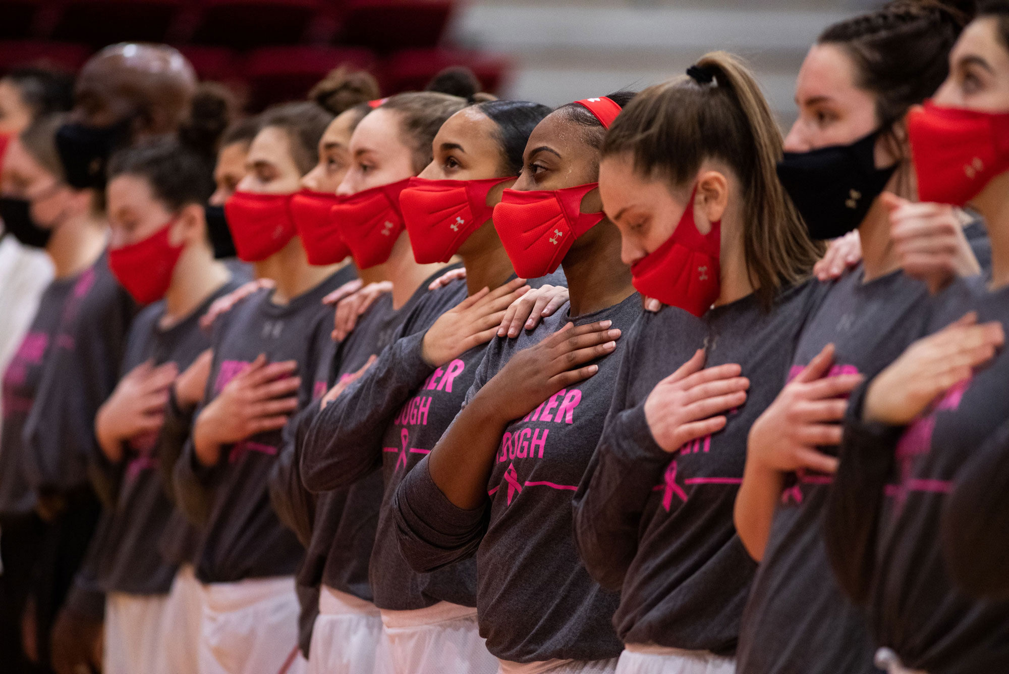 A photo of the BU women's basketball team wearing masks with their hands over their hearts before a game