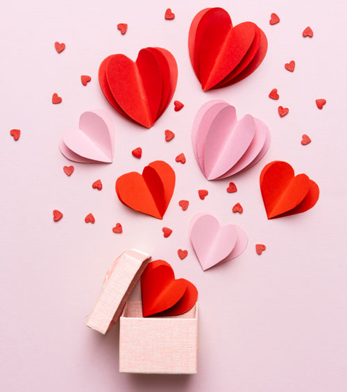 A photo of a pink box opening and red and pink hearts coming out of it along with confetti