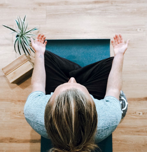 A photo taken from above or a woman sitting with her legs crossed, hands resting on her knees with palms upward