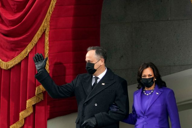 Phot of Vice President-elect Kamala Harris in a purple suit, looking slightly to her left, and her husband Doug Emhoff, turned to the right, in a black p-coat and black leather gloves. Emhoff waves as the two arrive for the inauguration of President-elect Joe Biden during the 59th Presidential Inauguration at the U.S. Capitol in Washington, Wednesday, Jan. 20, 2021.