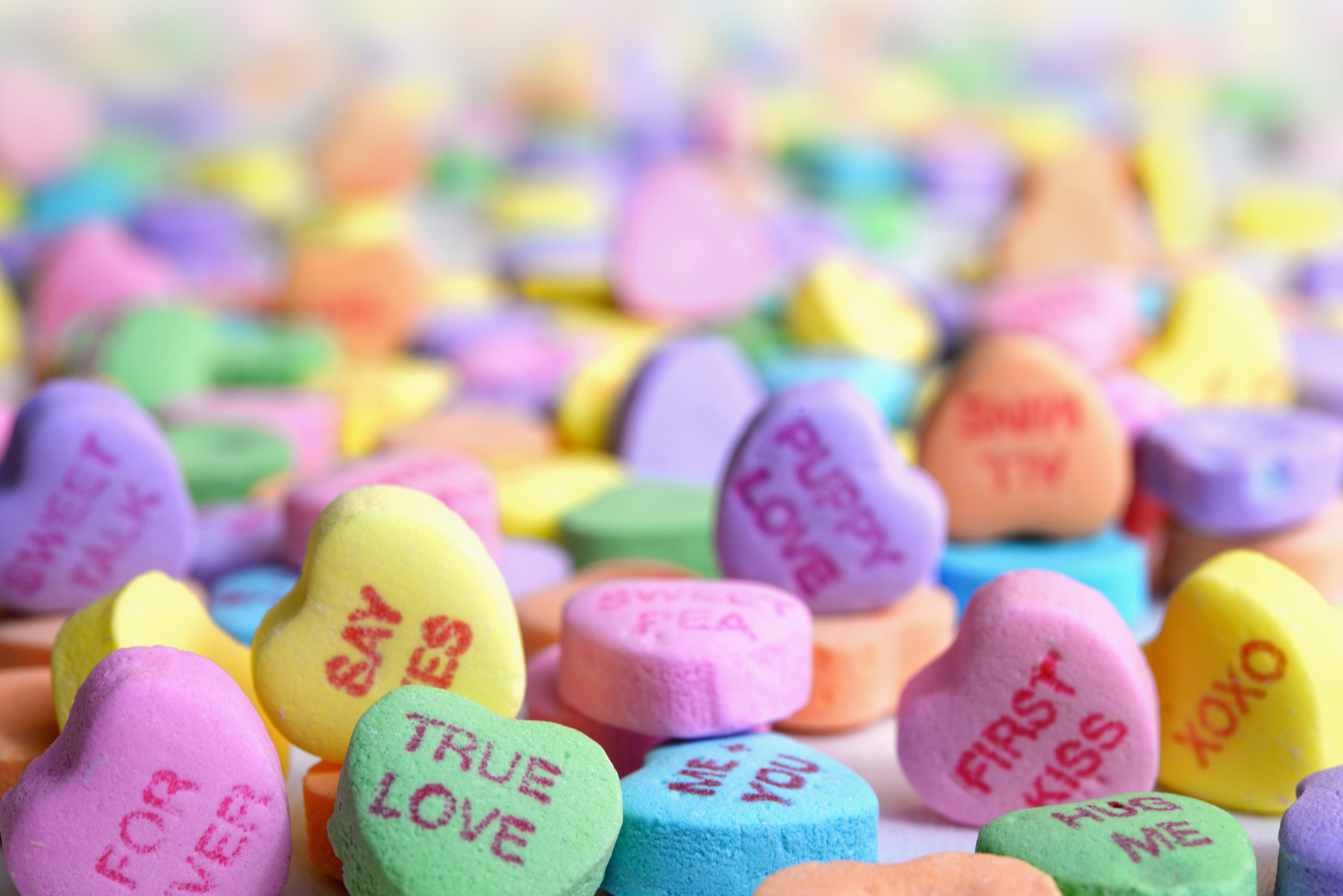 Photo of a pile of colored candy hearts that read phrases like "true love" and "say yes."