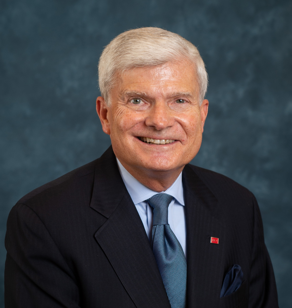 Headshot of Goldman School of Dental Medicine Dean Jeffrey Hutter smiling in a black suit jacket and blue tie, in front of dark blue background.