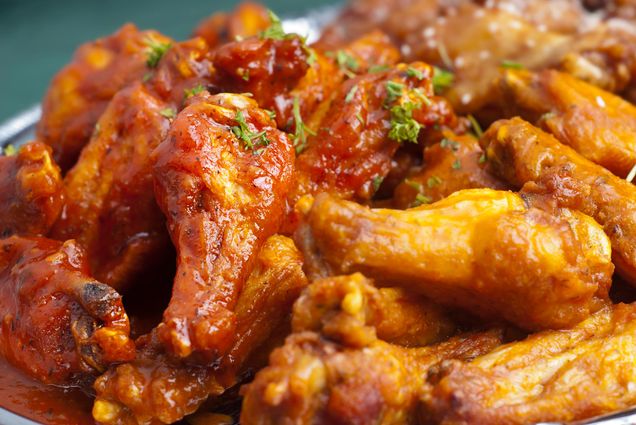 Image of a stack of Spicy Buffalo Chicken Wings, cover in an orangey, sticky sauce.