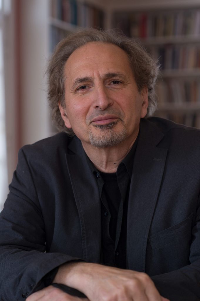 headshot of Pulitzer Prize winner Peter Balakian, who smiles slightly and crosses his hands; he wears a dark suit jacket. 