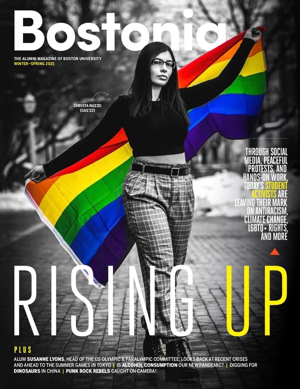 Cover for the Winter-Spring 2021 edition of Bostonia magazine. The issue is called "Rising Up" and the cover has a black and white photo of a student activist extending a pride flag behind her; the photo has been edited so the colors are shining through.