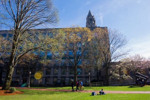 A photo of BU Beach behind CAS during spring. Several students are visible lounging on the grass.