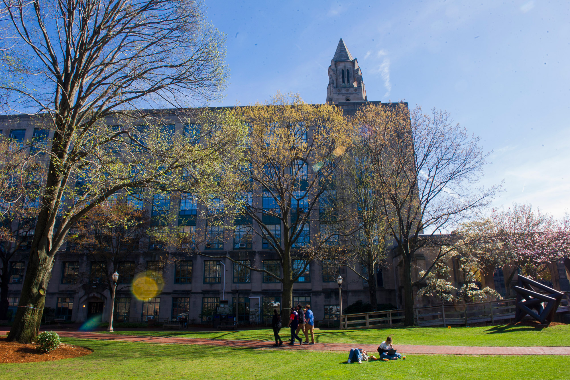 A photo of BU Beach behind CAS during spring. Several students are visible lounging on the grass.