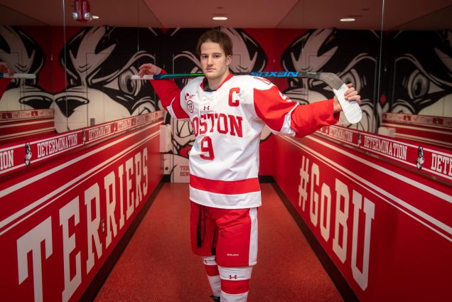 A photo of Logan Cockerill holding his hockey stick over his shoulders in the BU hockey dressing room