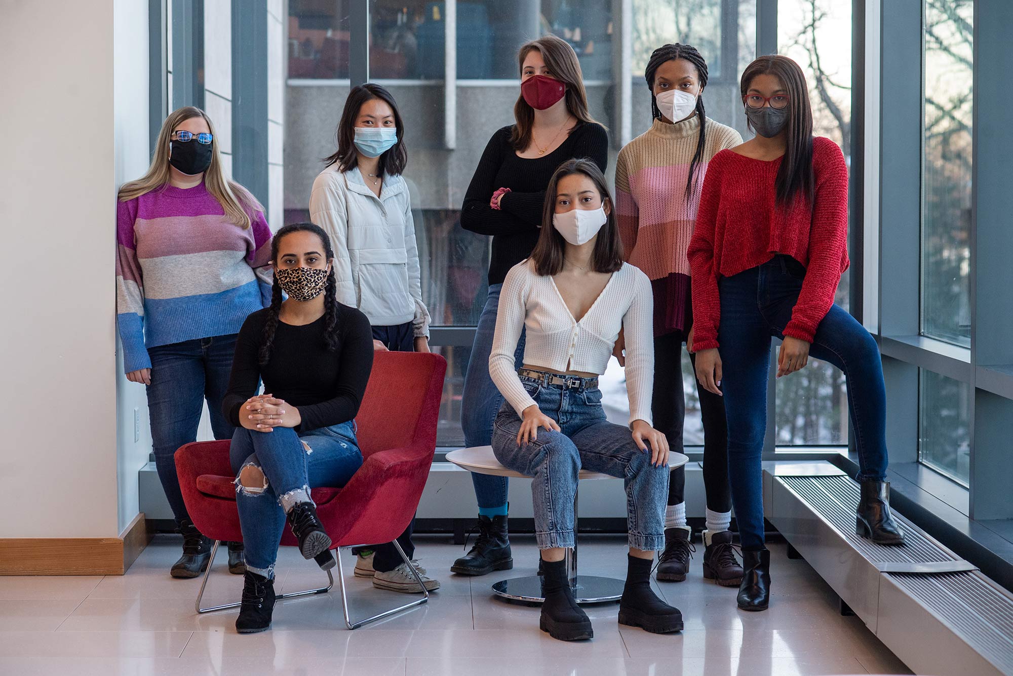 Photo of the students behind Migration Tales, from left, Jenna Hansen (CAS’23), Lara Werneck (CAS'23), Audrey Shen (Sargent’24), Iris Fitzsimmons Christensen (CGS’21, CAS’23), Lauren Mai (CAS’22), Safiya Umrani (CAS’23), and Auroramary Estaba (CAS’22). The group stands or sits at the end of a hallway with a window behind them; they all wear face masks and stylishly dressed, many in sweaters.