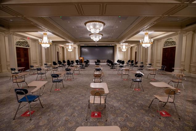 Photo of a classroom is set-up in one of the ballrooms at 1 Silber Way, the desks are spaced six feet apart and have red stickers underneath to indicate social distancing guidelines. Six fancy chandeliers hang from the ceilings.