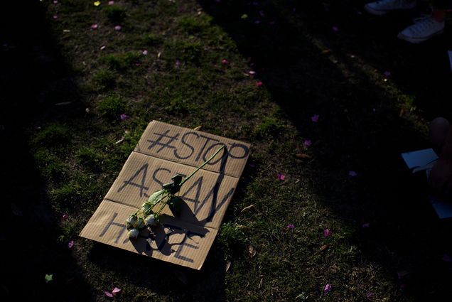 Photo of a sign laid on the grass during a Stop Asian Hate rally at Discovery Green in downtown Houston, Texas on March 20, 2021. A flower is laid across the cardboard sign that reads “#Stop Asian Hate” in black sharpie.