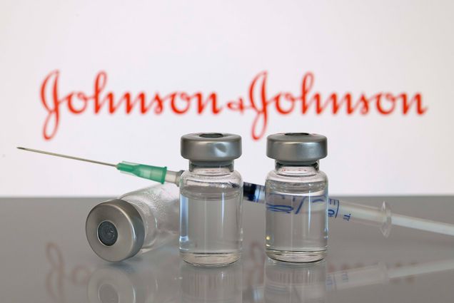 Photo of three clear glass vials with silver covers and a syringe with the words “Johnson & Johnson” in red in the background.