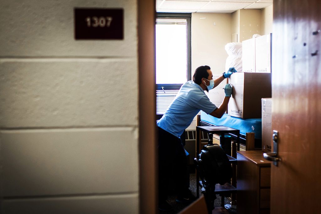 Photo of Tsewang Gyalpo of BU Facilities as he packs up a student’s dorm room in Sleeper Hall, July 2020. Photo is taken from the hallway, Gyalpo is framed by the door, as he writes on one of the cardboard boxes.