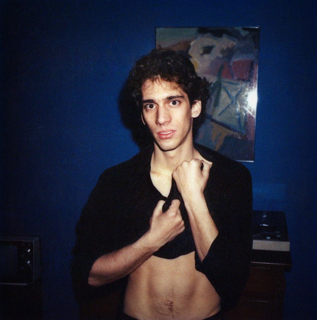 Film photo of Michael Grecco (COM’81) at his apartment in the Back Bay, circa 1980. He pulls his black shirt up exposing his stomach.