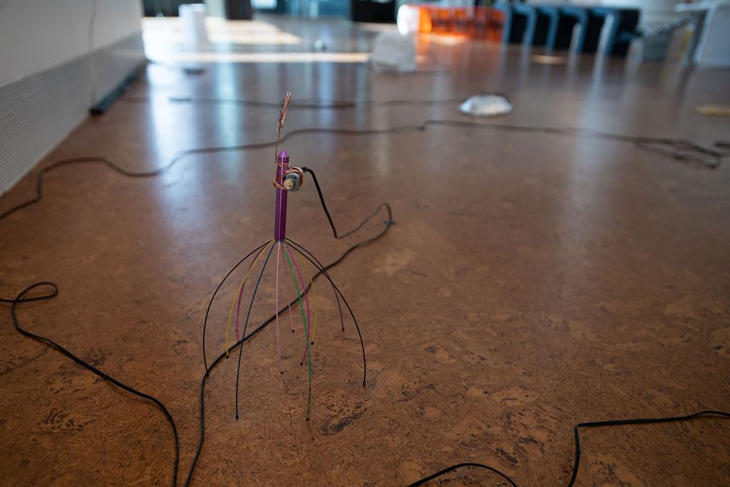 Photo of an element of Chang Wu’s (MFA’20) sculpture, “The Stuff -As -Dreams Are Made -On. The sculpture looks like a scalp massager, and rests on the ground of the gallery surrounded by black wires.