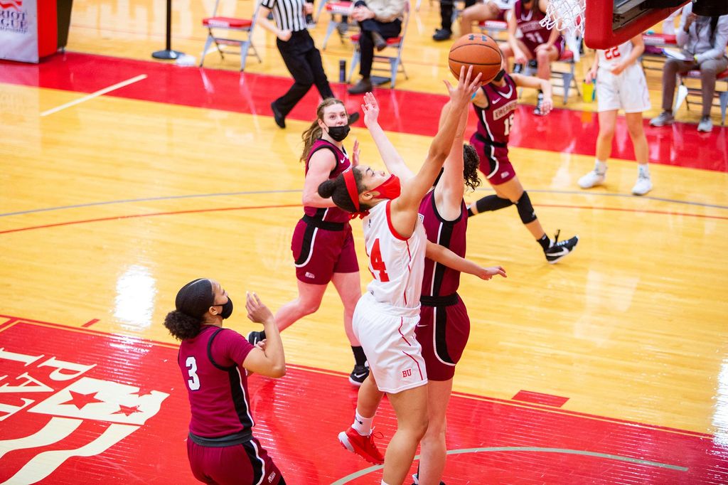 Photo of Sydney Johnson (CAS’23) going up for a lay up as defenders in crimson try to block her shot.