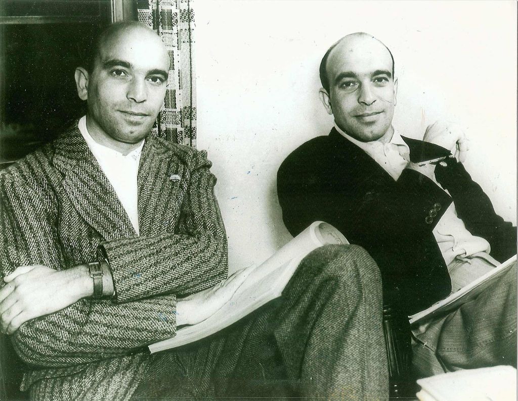 Black and white photo of Julius Epstein (left) and Philip Epstein. The two brothers sit with their backs against a wall, they wear thick, striped suits and hold what look like printed screenplays in their laps and smile slightly.