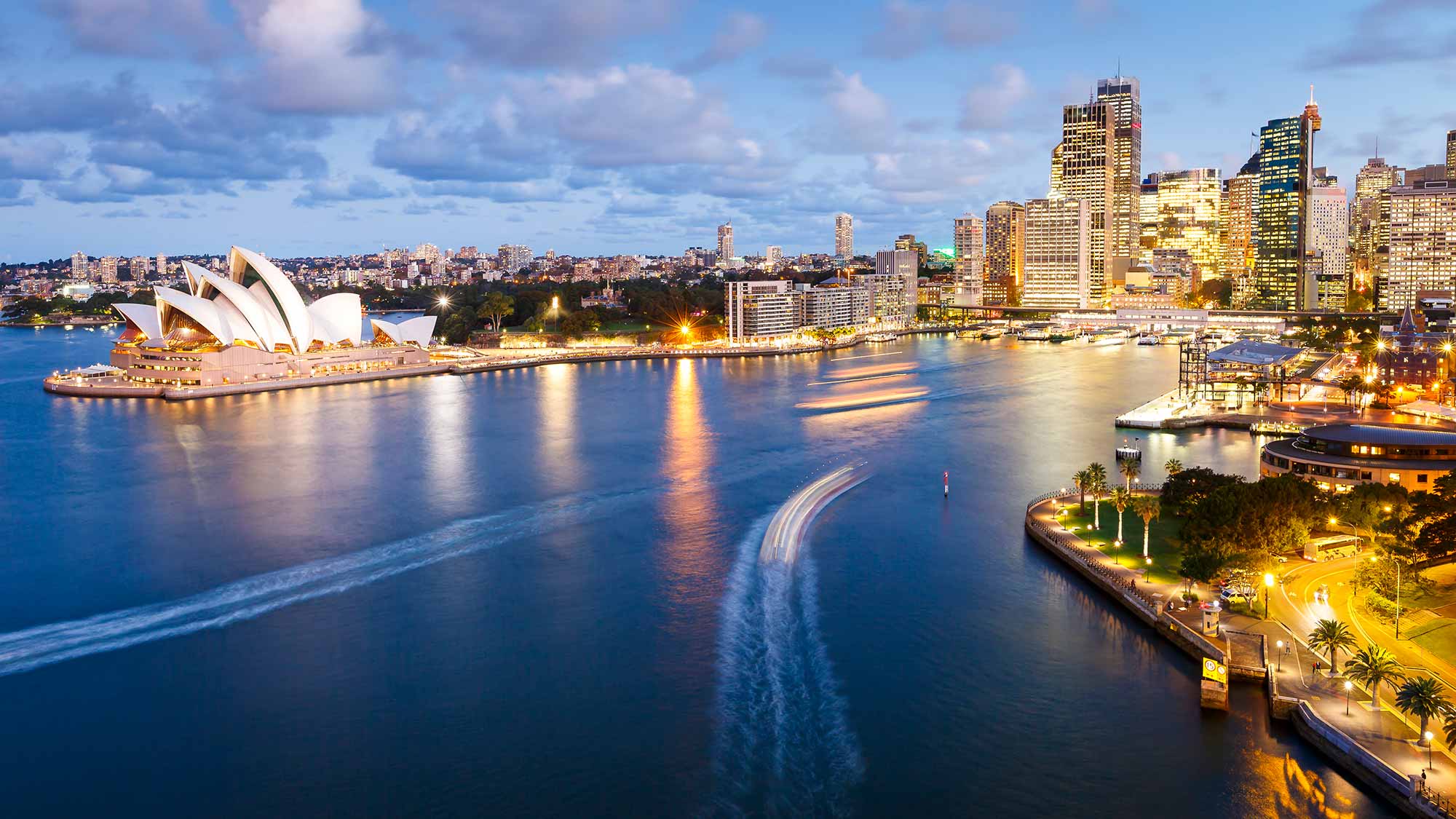 The Circular Quay neighborhood in Sydney, Australia taken from the Sydney Harbour Bridge just after sunset showing the Sydney Opera House on the left.