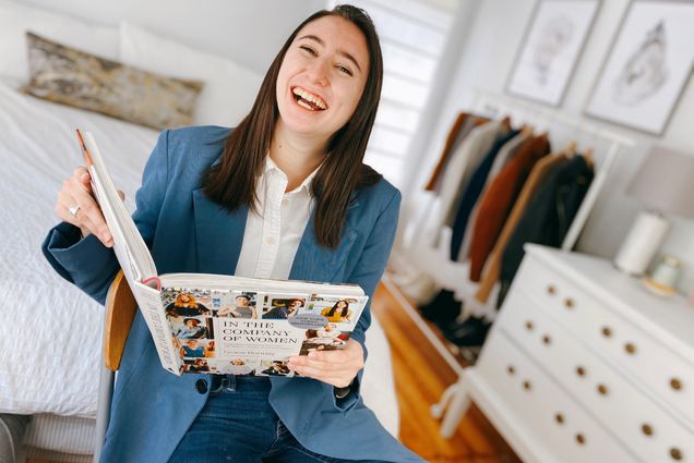 A photo of Sarah Greisdorf holding a book open and laughing