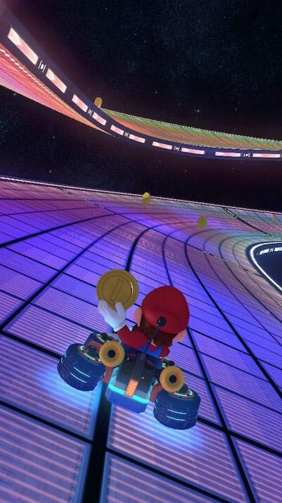 A photo of Mario Kart. Mario is visible in his kart holding a coin on the Rainbow Road level.