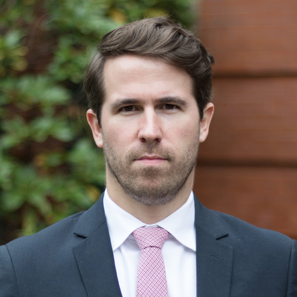 Headshot of Michael Ulrich in a black suit and pink tie looking concentratedly towards the camera.