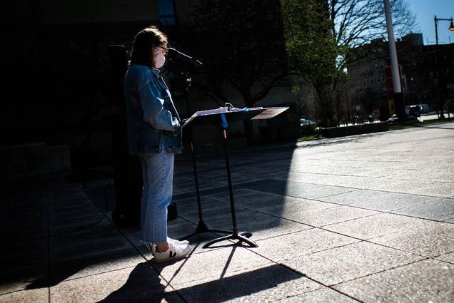Olivia Ritter (COM 21) reads the names of the Holocaust victims on Marsh Plaza during Yom HaShoah — Holocaust Remembrance Day on April 8, 2021. Ritter wears jeans and a jean jacket and stands partially in the shadow of a nearby building.