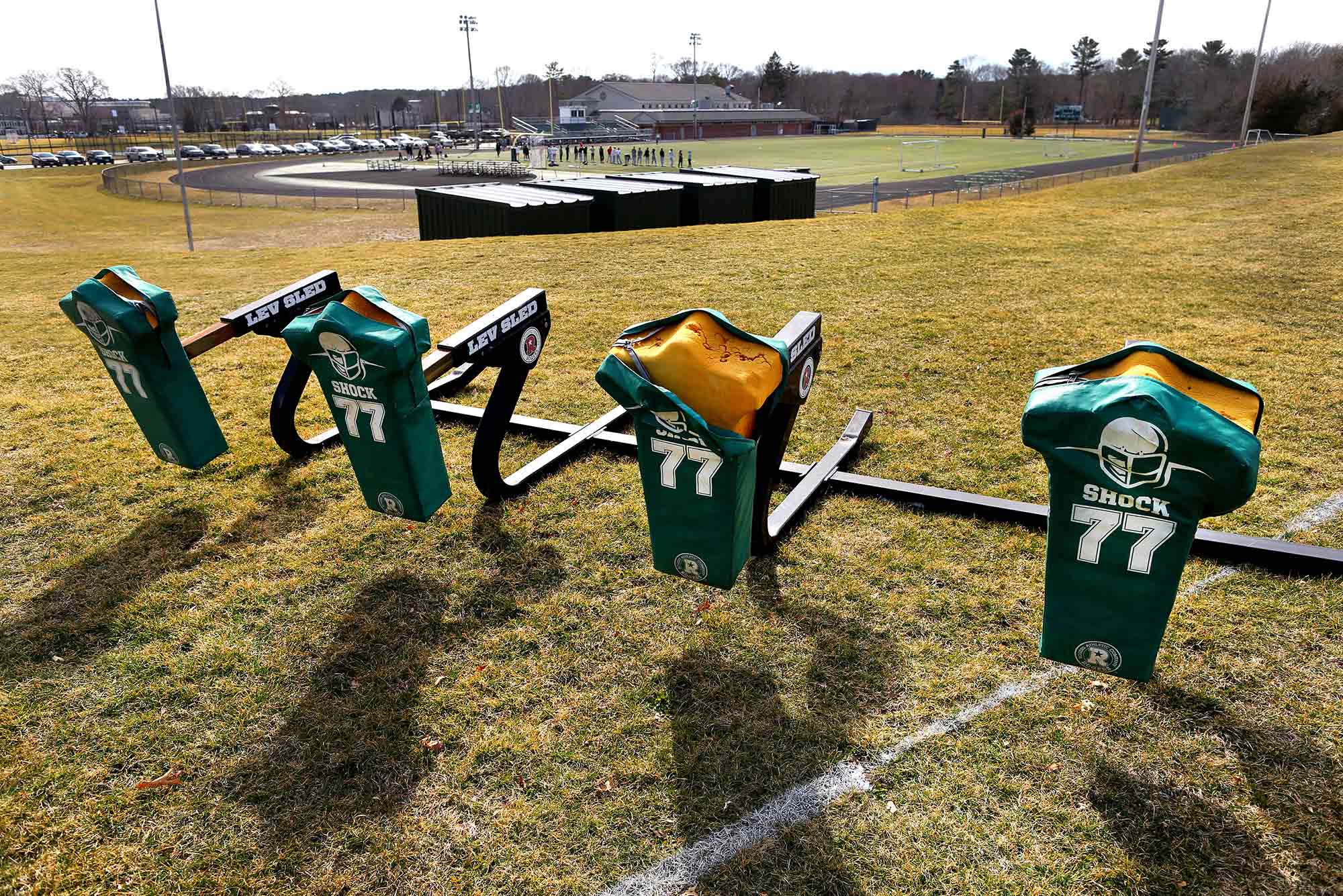 Photo of a football push sled with green number 77 jerseys on it in a field on Duxbury high school's grounds.
