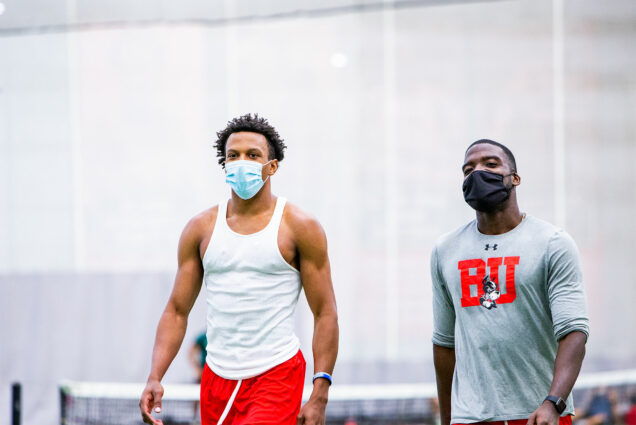 Photo of Kasim Cisse (CAS’22) (left), in a white tank top and red shorts, and Emeka Ibeh (Questrom’21), in a gray BU athletics long sleeve, walking side by side. They wear face masks.