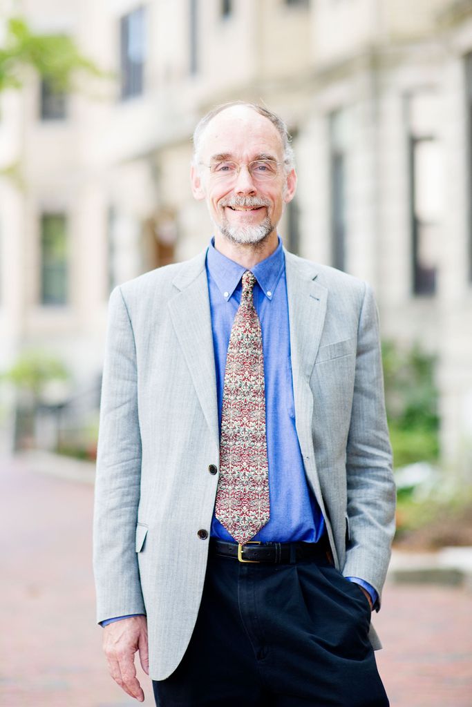 Headshot of Karl Kirchwey, CAS Professor and the Director of Creative Writing, he stands with his hand in his pocket and smiles. He wears a gray suit jacket, blue button down, and colorfully patterned tied. 