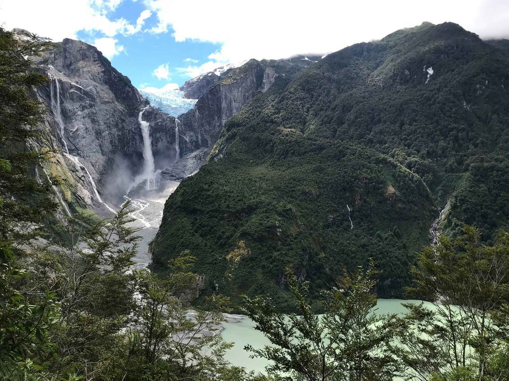 Photo of Patagonia with large green mountains and a waterfall in the distance.
