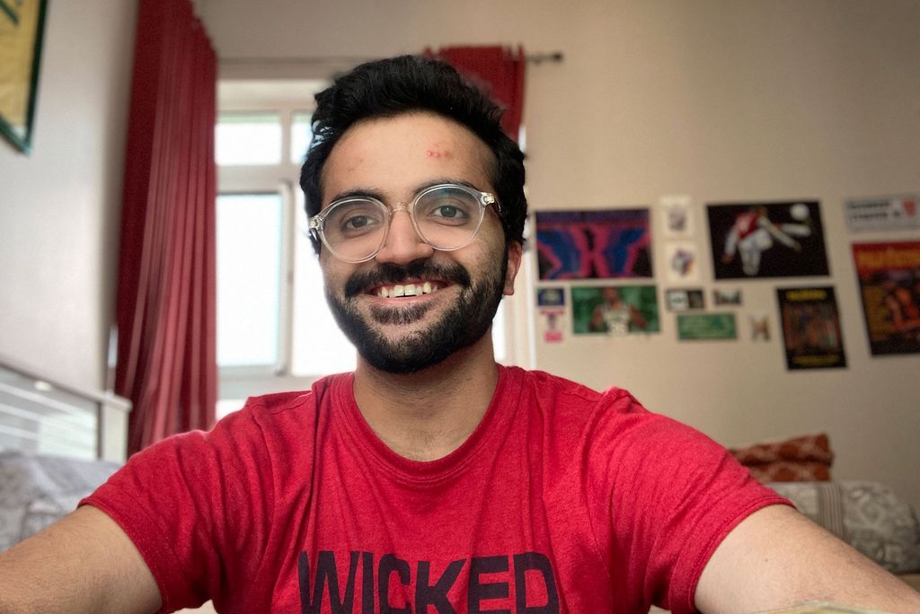 Photo of Shubhankar Arun (COM’20) in a red shirt that says "Wicked", smiling as he sits in what looks like his bedroom.