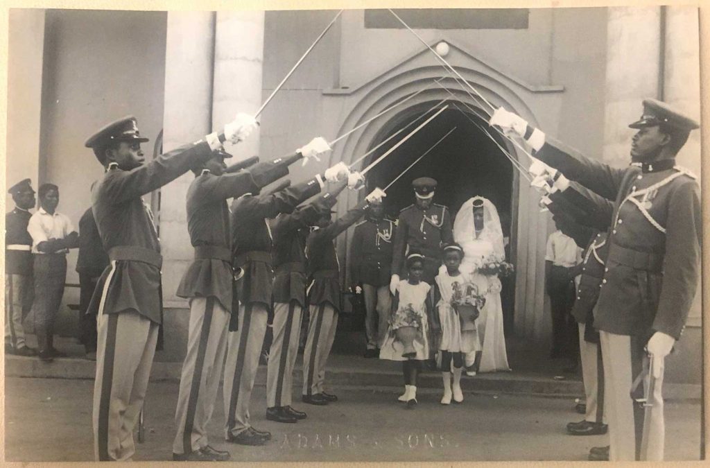 Photo from the wedding of Louis Chude-Sokei’s parents in Lagos, Nigeria, 1963. They are exiting the chapel through a row of guards in military dress holding swords in a rooftop formation over the couple.