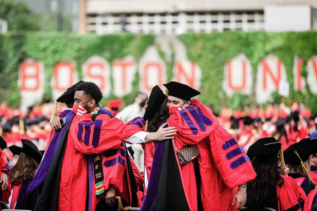 Two pairs of graduating Advanced Degree Students hug each other at the 2021 BU Commencement ceremony for graduate students.