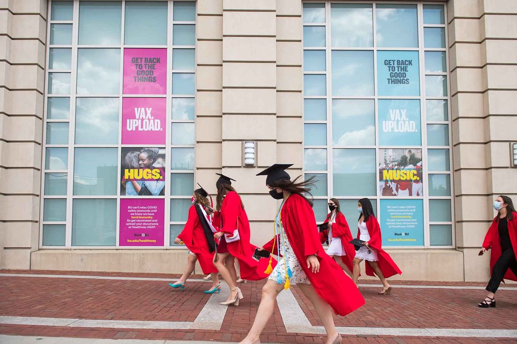 A group of graduates wearing caps and gowns flowing in the breeze walk up Commonwealth Ave towards Nickerson Field for the undergraduate Commencement ceremony.