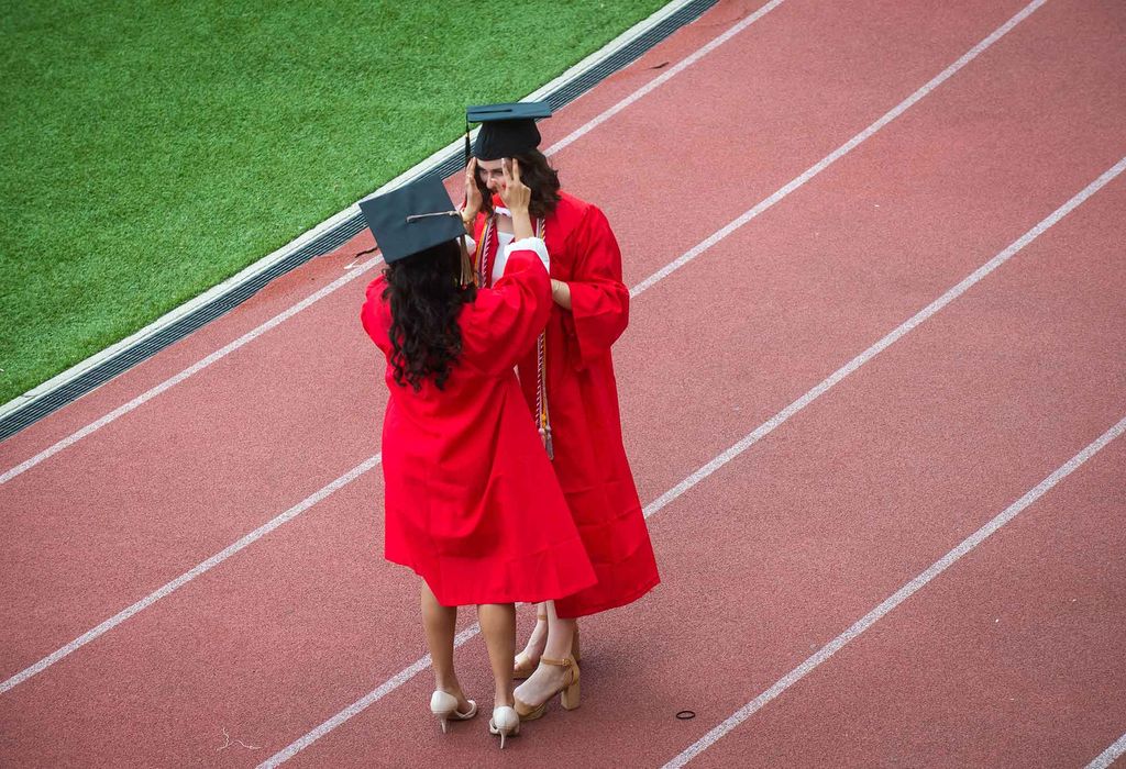 A graduate stops to fix the mortarboard cap and hair of another graduate on the track at Nickerson Field during Commencement.