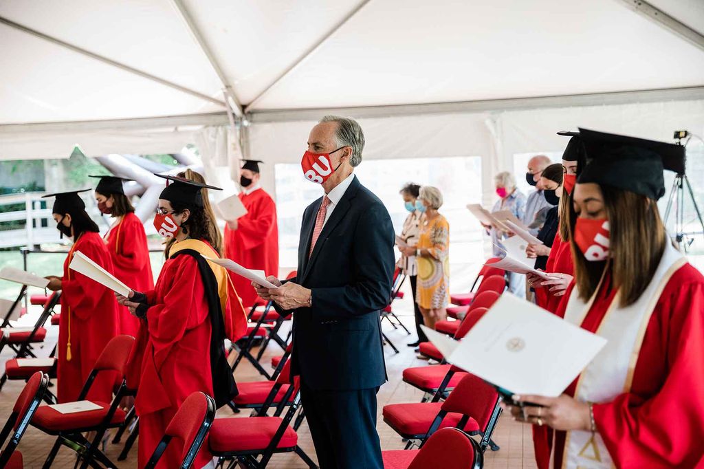 Graduating students in cap and gowns and attendees stand participating in the Marsh Chapel Baccalaureate Service during Boston University's 148th Commencement, Sunday, May 16, 2021.