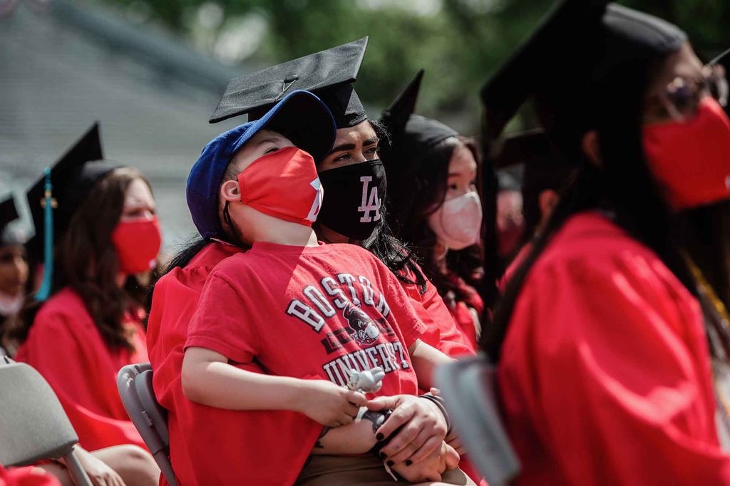 A graduate holds a child as they watch the undergraduate Commencement ceremony on Nickerson Field.