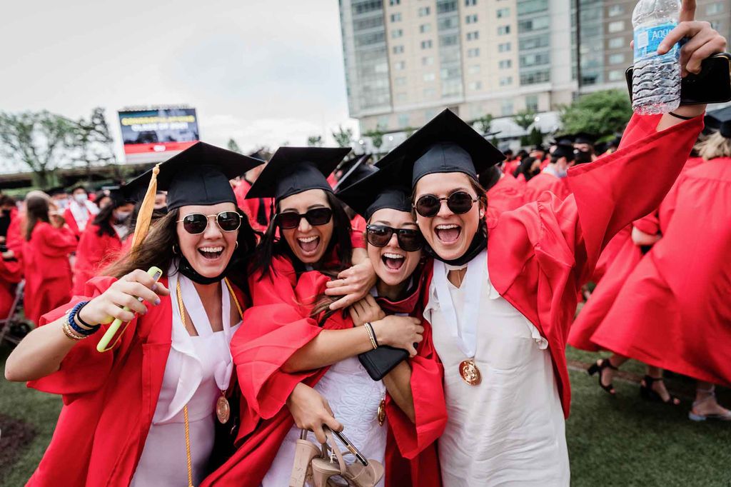 4 graduates wrap their arms around each other and cheer posing for a photo following Commencement.