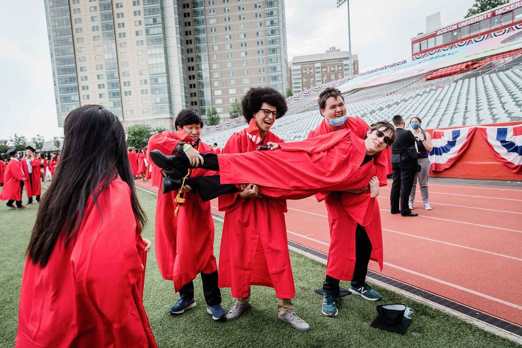 Three graduates hold their friend sideways in the air for a photo on Nickerson Field