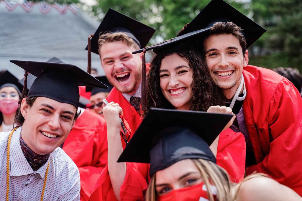 5 graduates wearing their black mortarbord caps smile for a photo.