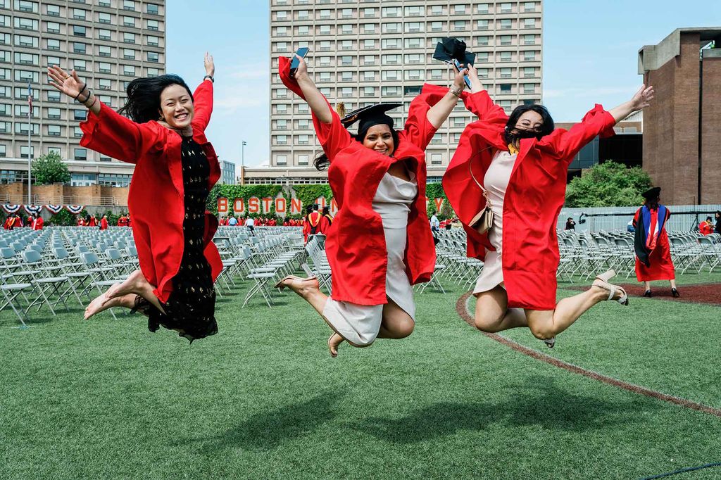 3 graduating students wearing caps and gowns jumping in the air on Nickerson Field