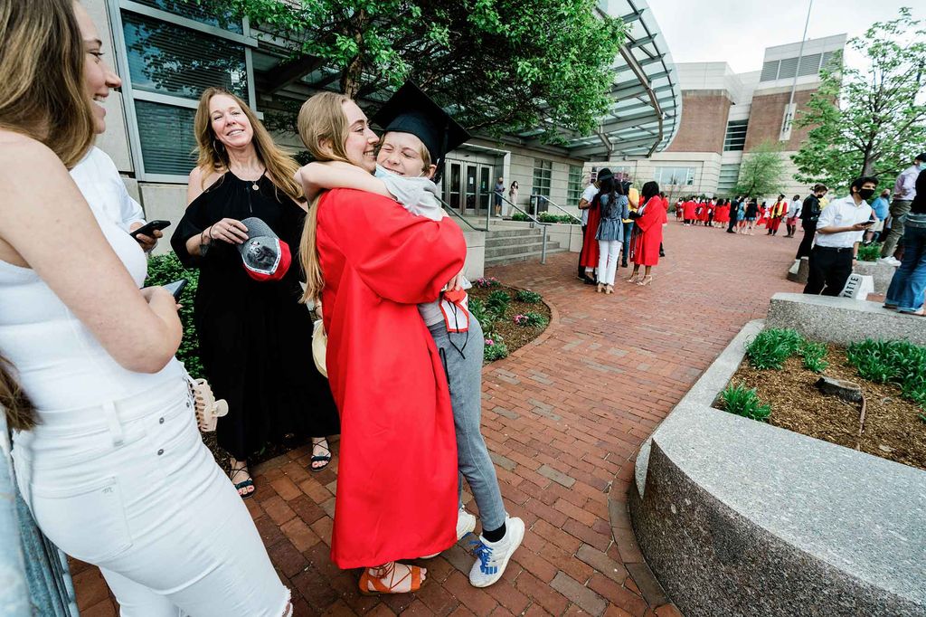 A graduating student wearing her red graduation robe gives a big hug to a younger family member.